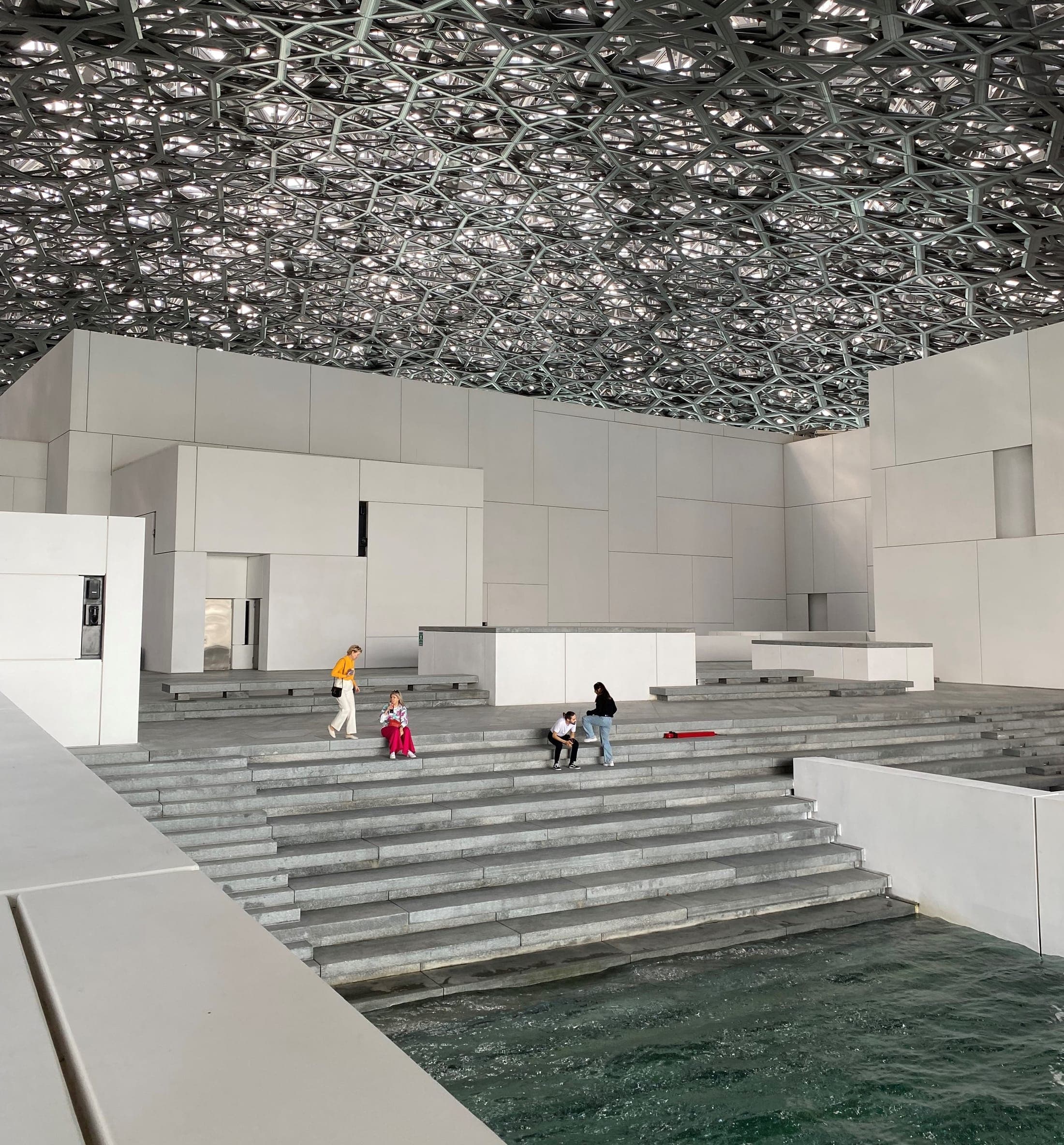 Louvre Abu Dhabi dome reflected over water with dappled light